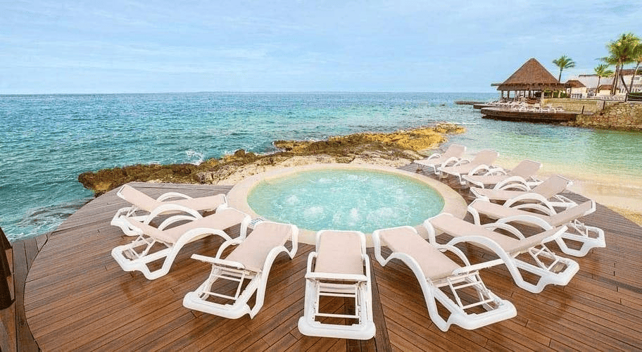 a hot tub surrounded by chairs on a deck overlooking the ocean