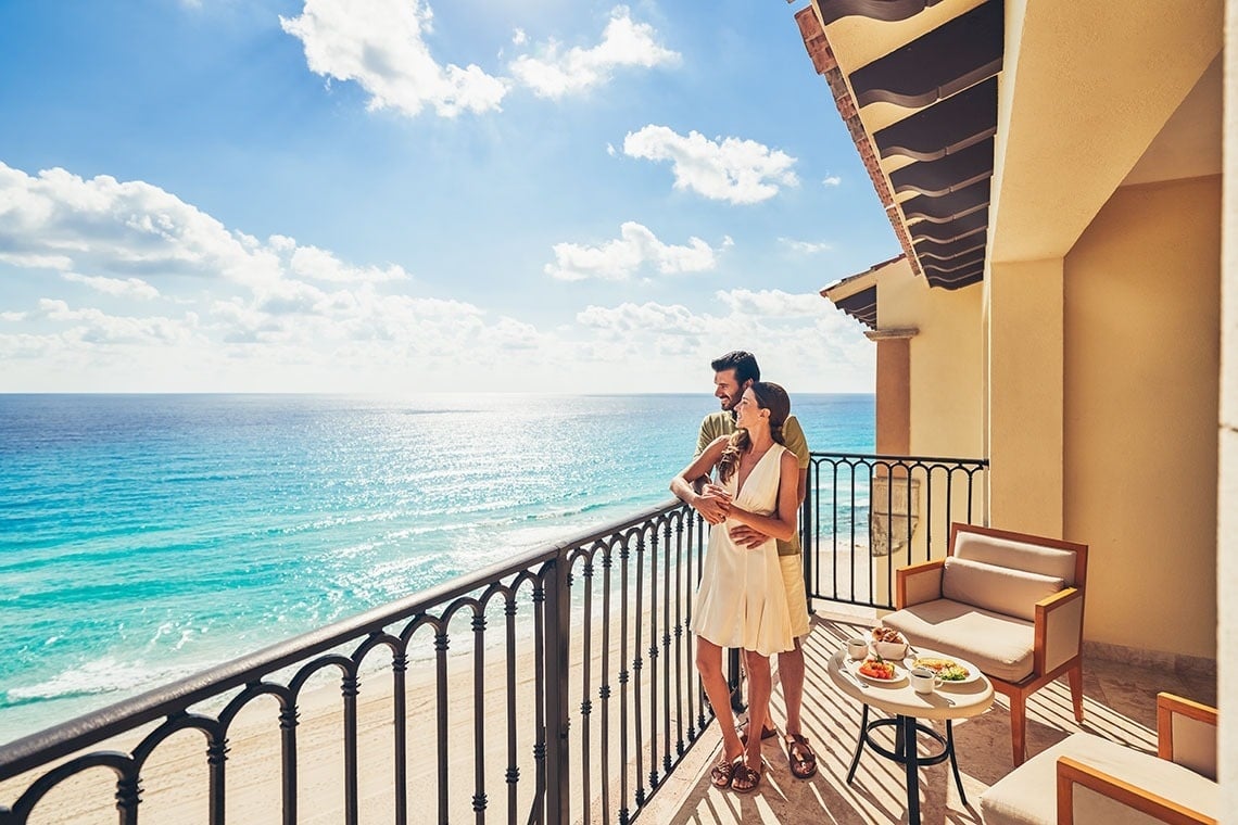 a man and woman standing on a balcony overlooking the ocean
