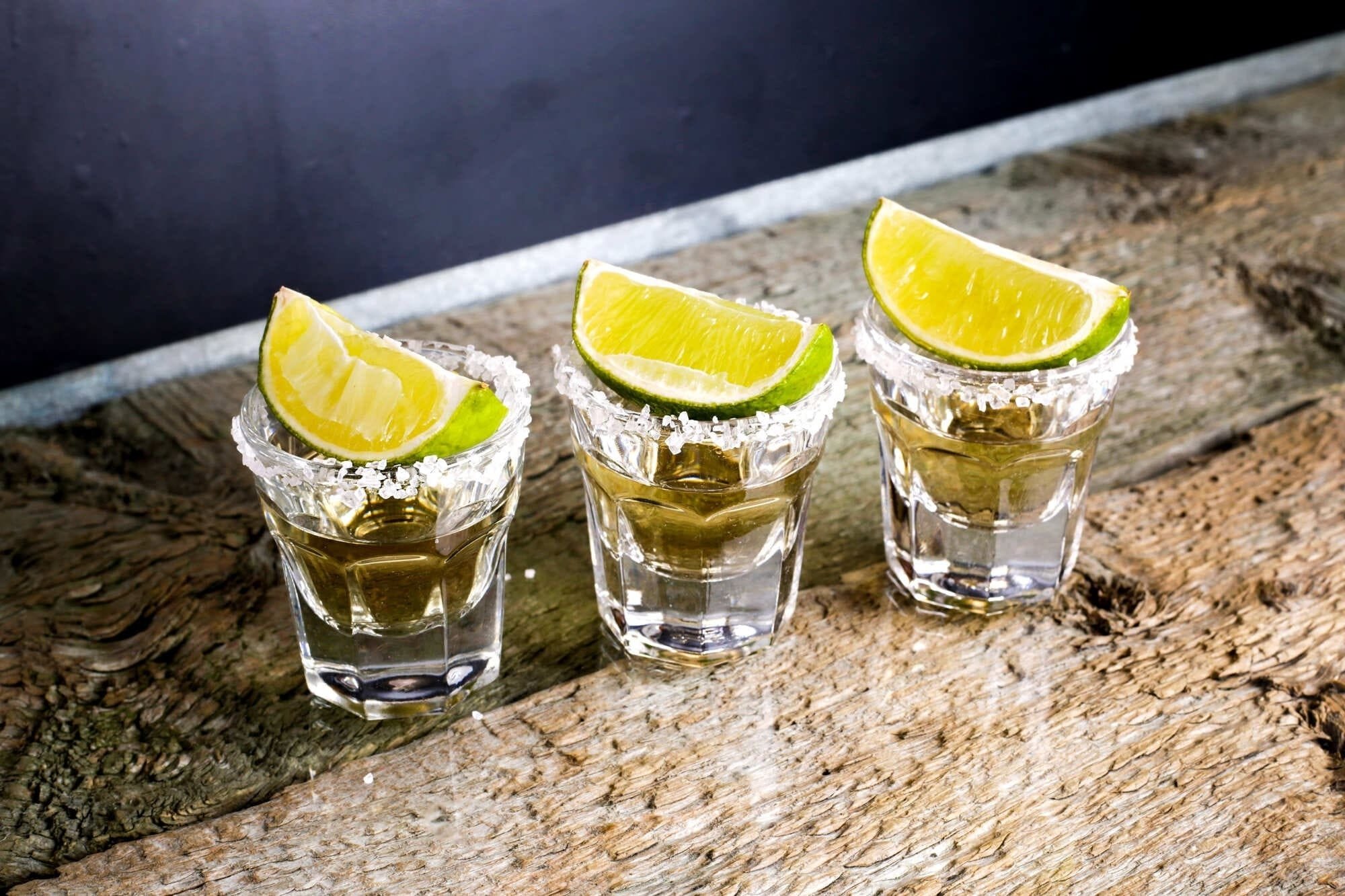 tres vasos de tequila con rodajas de limón sobre una mesa de madera