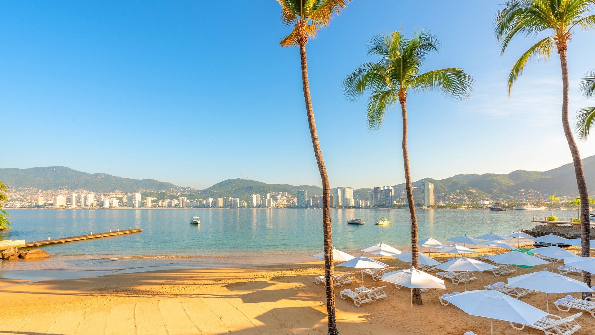 Beach with umbrellas, seats and palm trees of the Hotel Park Royal Beach Acapulco