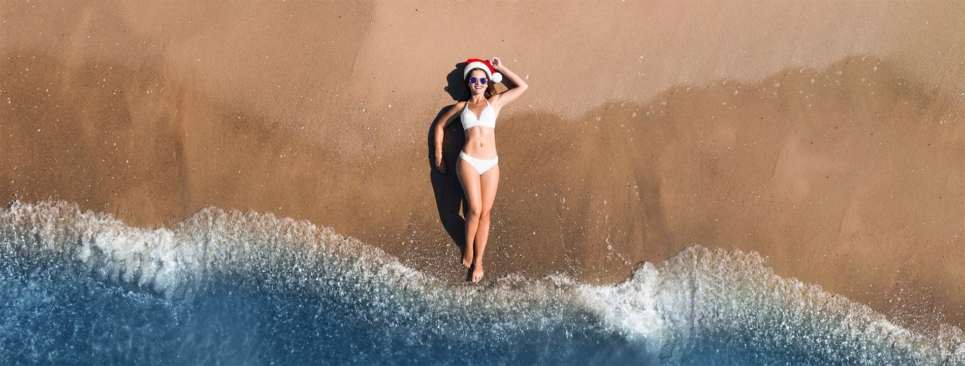 uma mulher de biquíni e chapéu de papai noel está deitada na praia