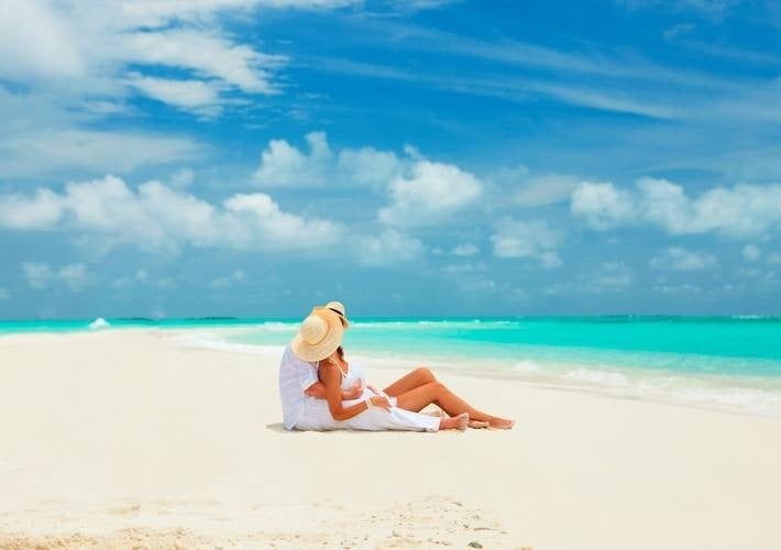 a man and woman are sitting on the beach looking at the ocean