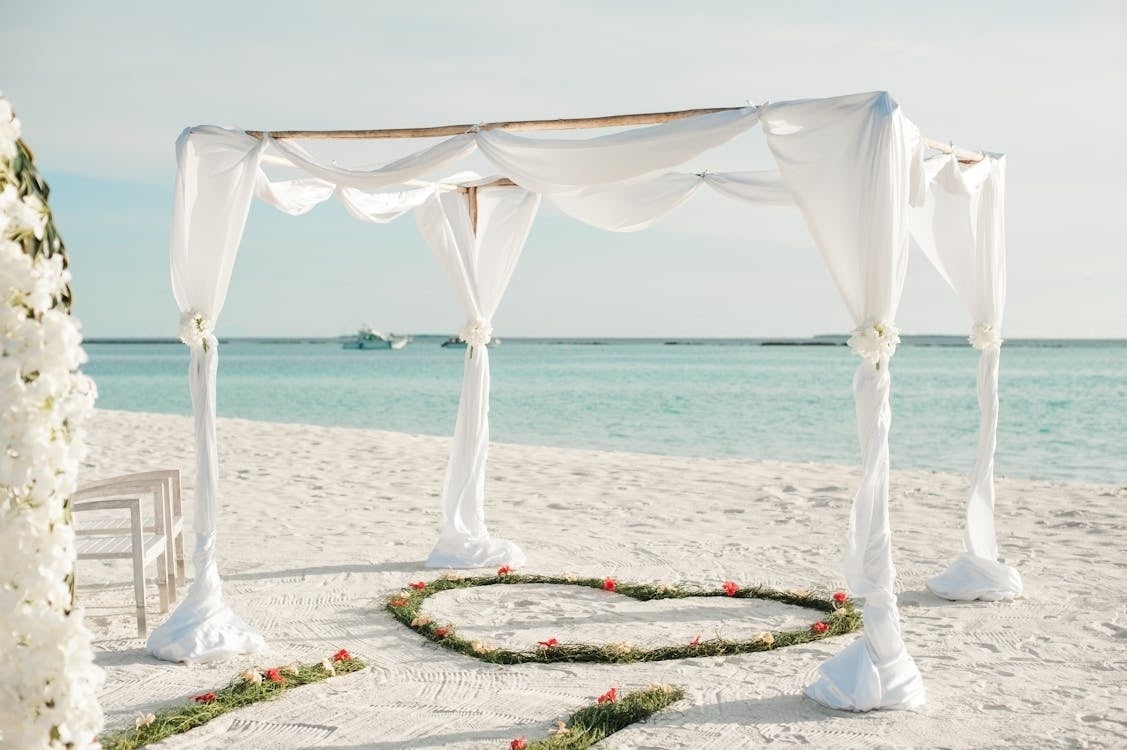 uma praia com um gazebo branco e um coração de flores na areia