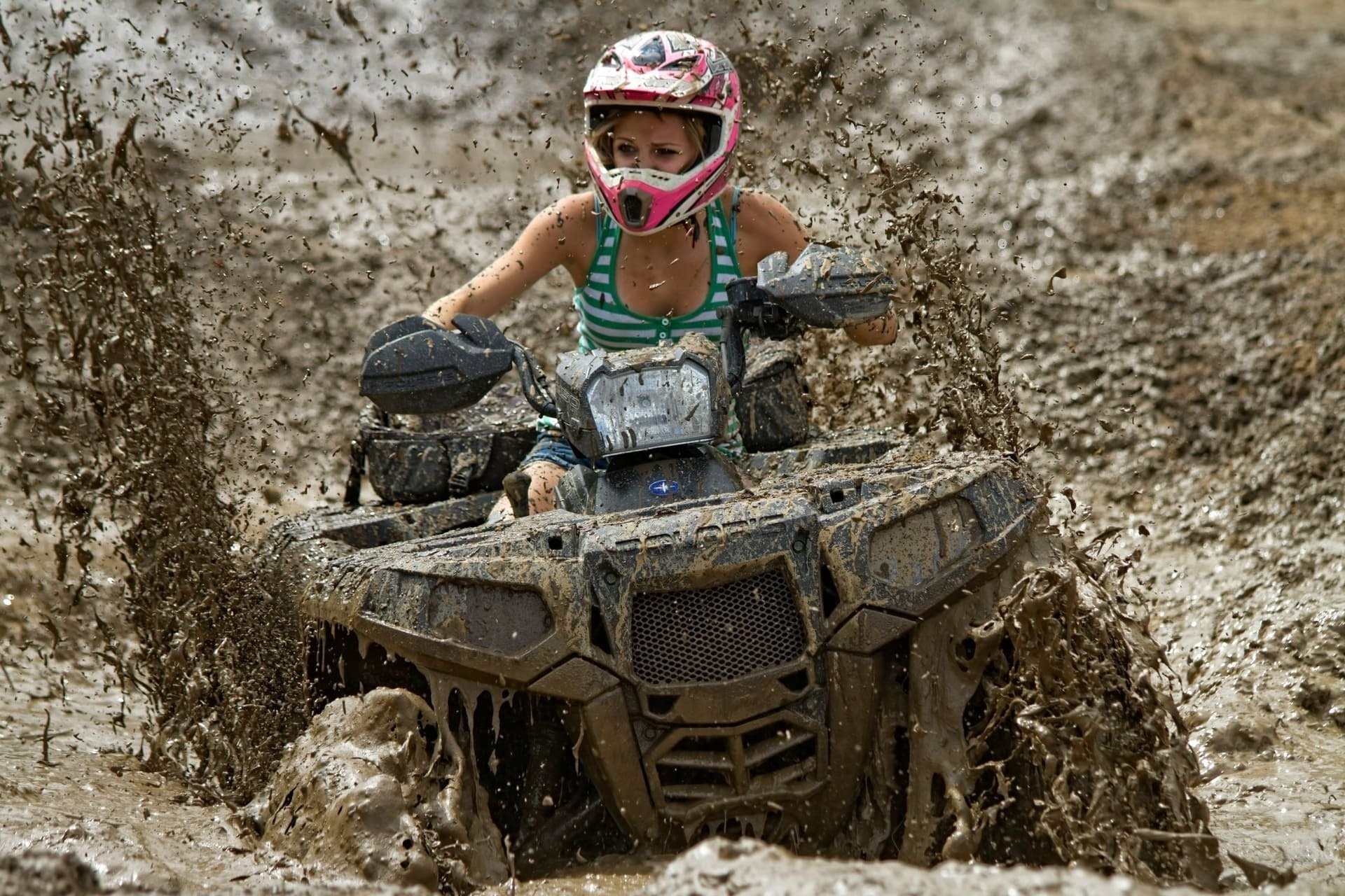 a woman wearing a pink helmet is riding a muddy atv