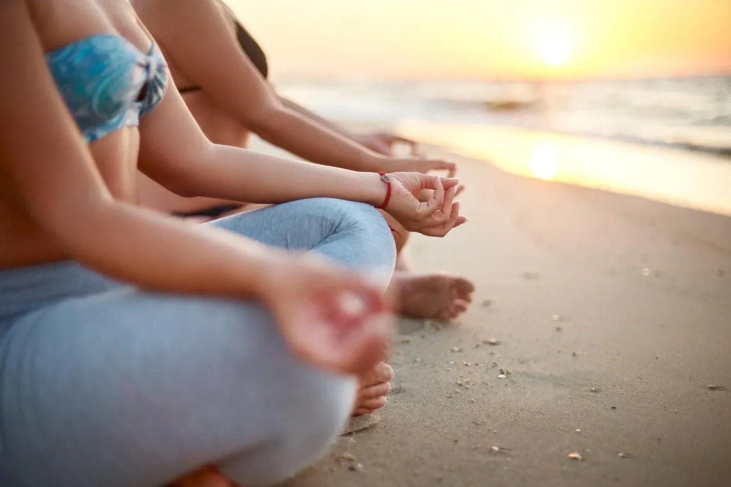 un grupo de mujeres están sentadas en una pose de yoga en la playa al atardecer