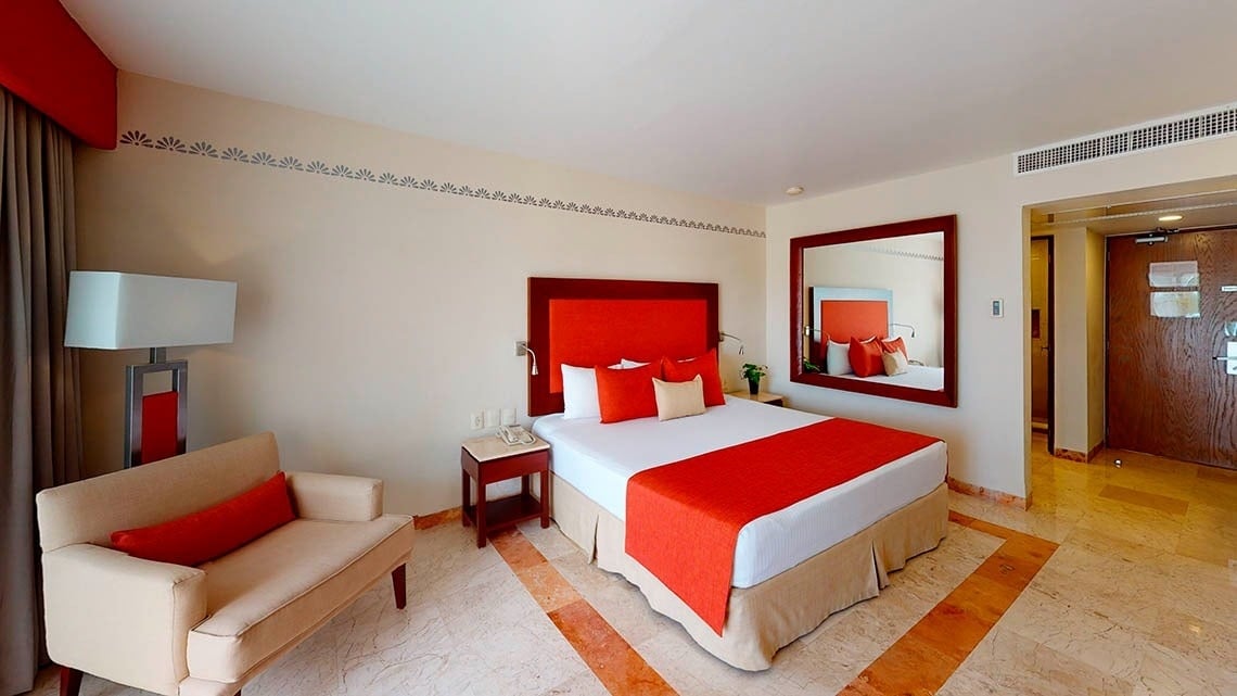 Quarto com cama king size, mesa de cabeceira e poltrona no Grand Park Royal Cancun Hotel