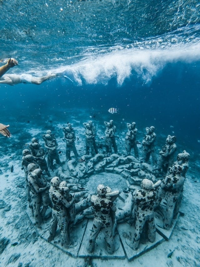 a woman is swimming in the ocean near a circle of statues