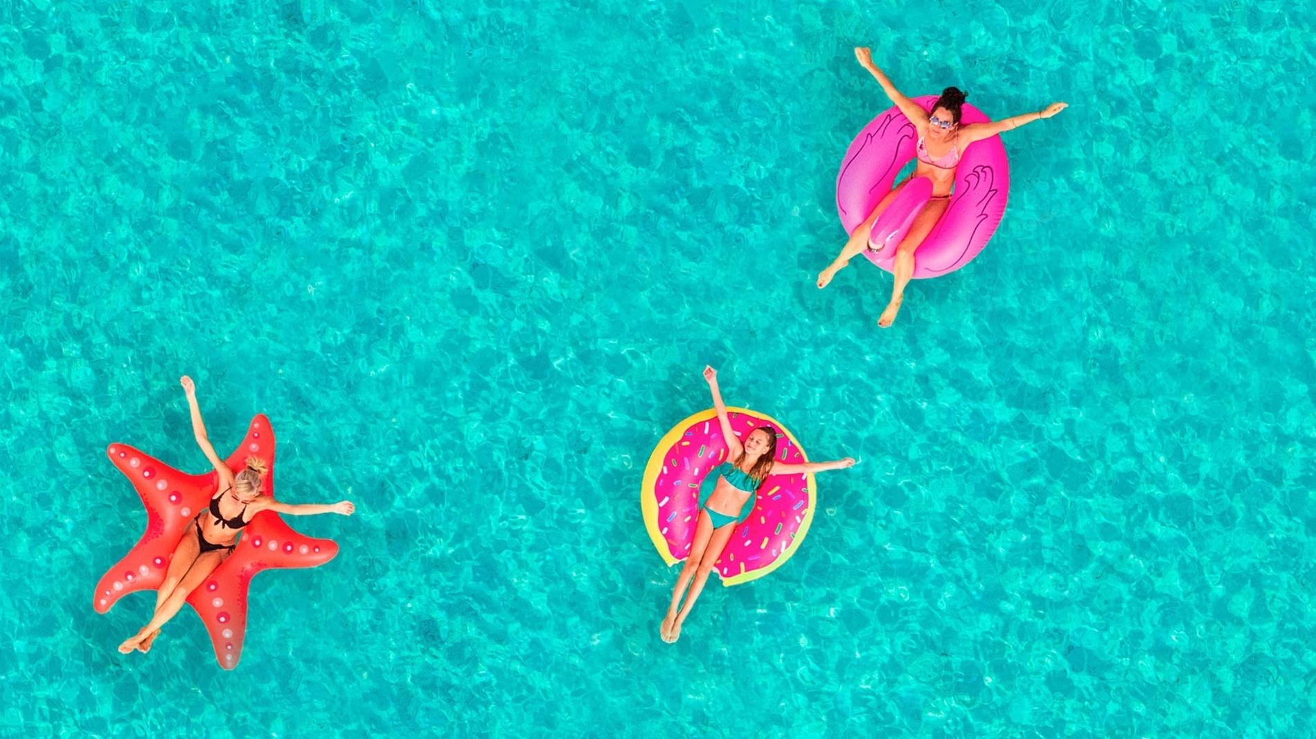 una vista aérea de tres mujeres flotando en anillos inflables en el agua .