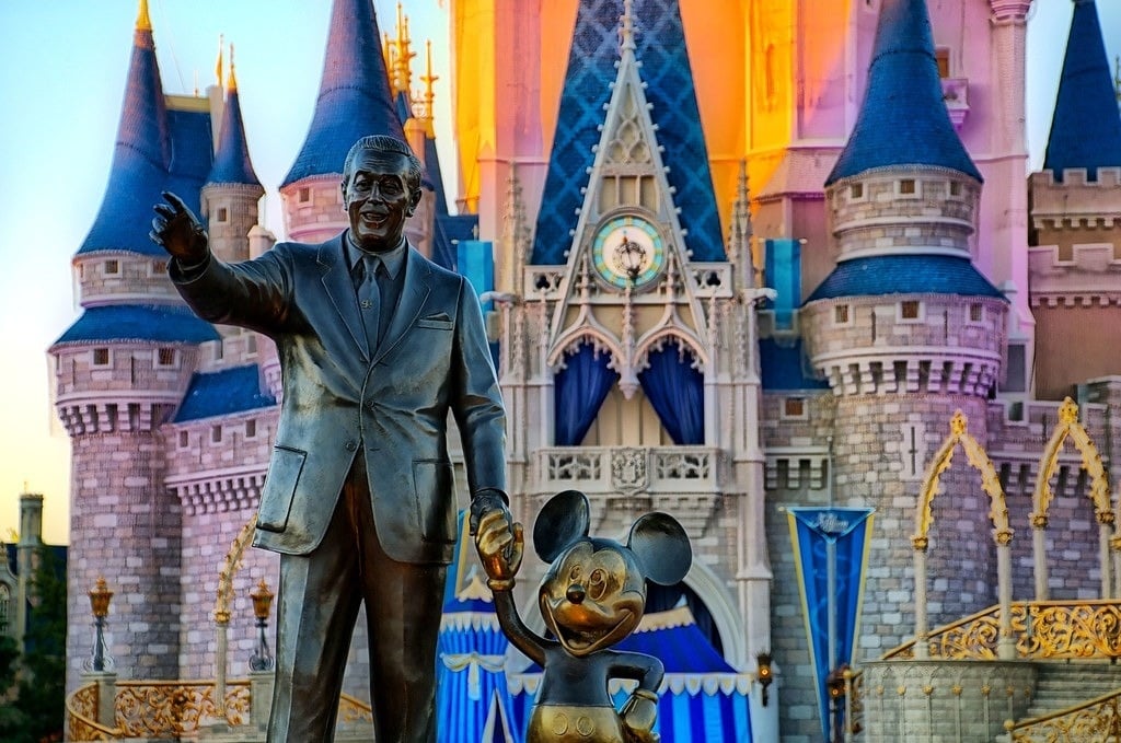 una estatua de walt disney y mickey mouse frente al castillo de cenicienta