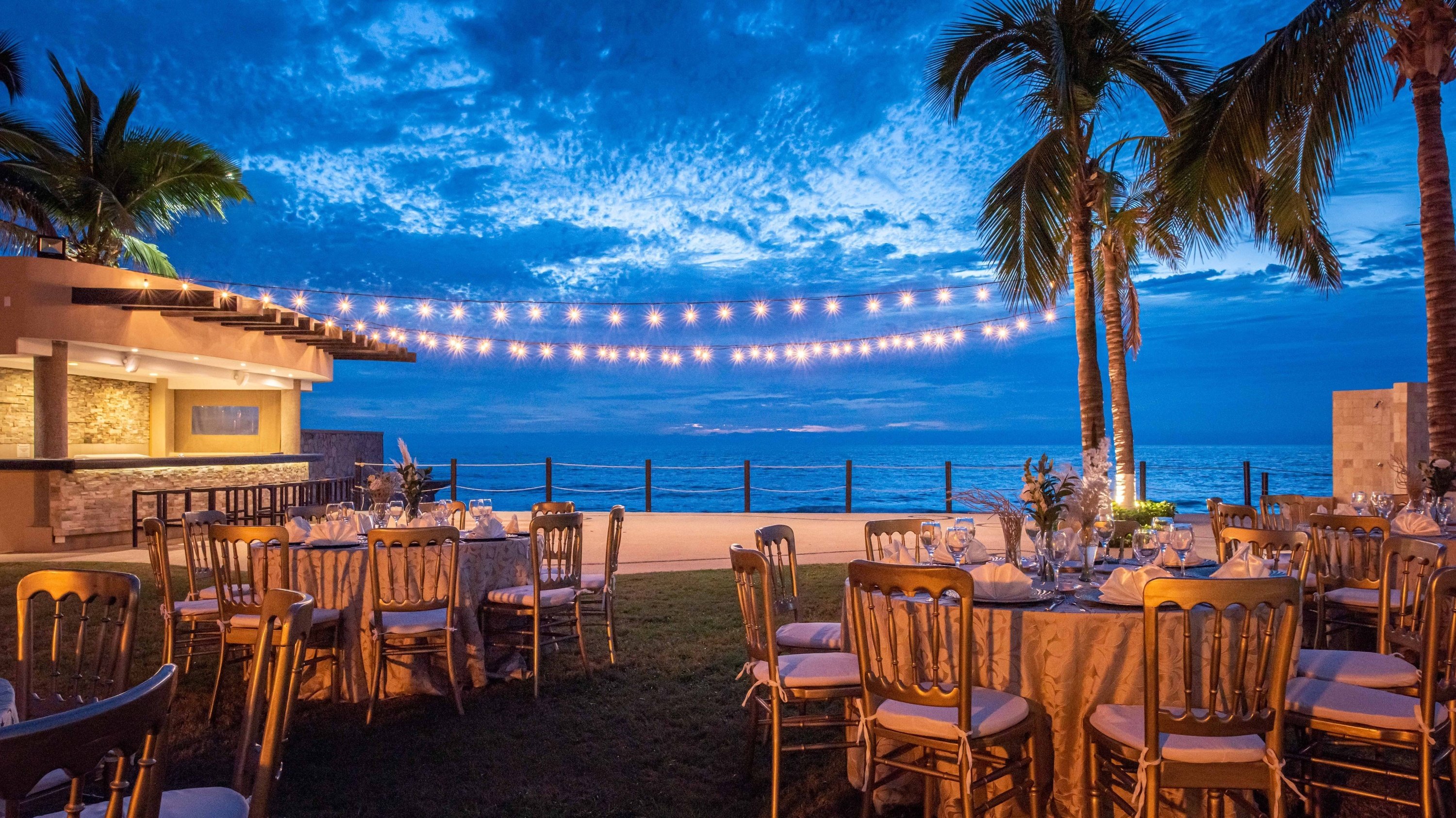 Relaxation area with Balinese bed, tables, lights and beach at sunset of the Grand Park Royal Cancun Hotel