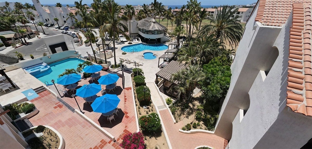 an aerial view of a resort with a large pool and blue umbrellas