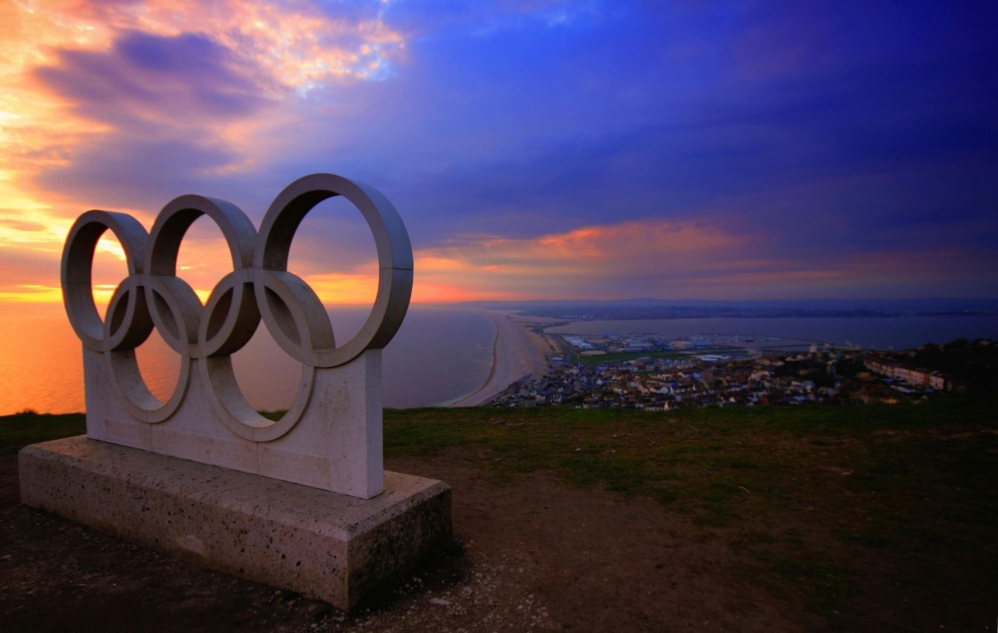 uma estátua de anéis olímpicos com o pôr do sol ao fundo