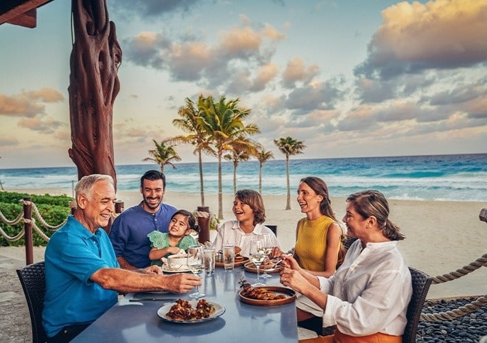 una familia se sienta en una mesa en la playa comiendo