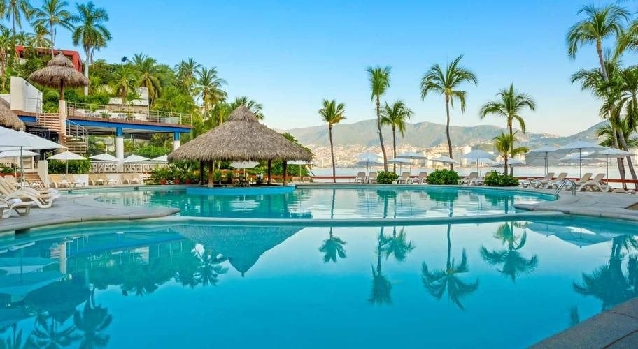 Piscina exterior con vista al mar y bar con tejado de palma del Hotel Park Royal Beach Acapulco