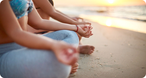 un grupo de mujeres están sentadas en una pose de yoga en la playa al atardecer