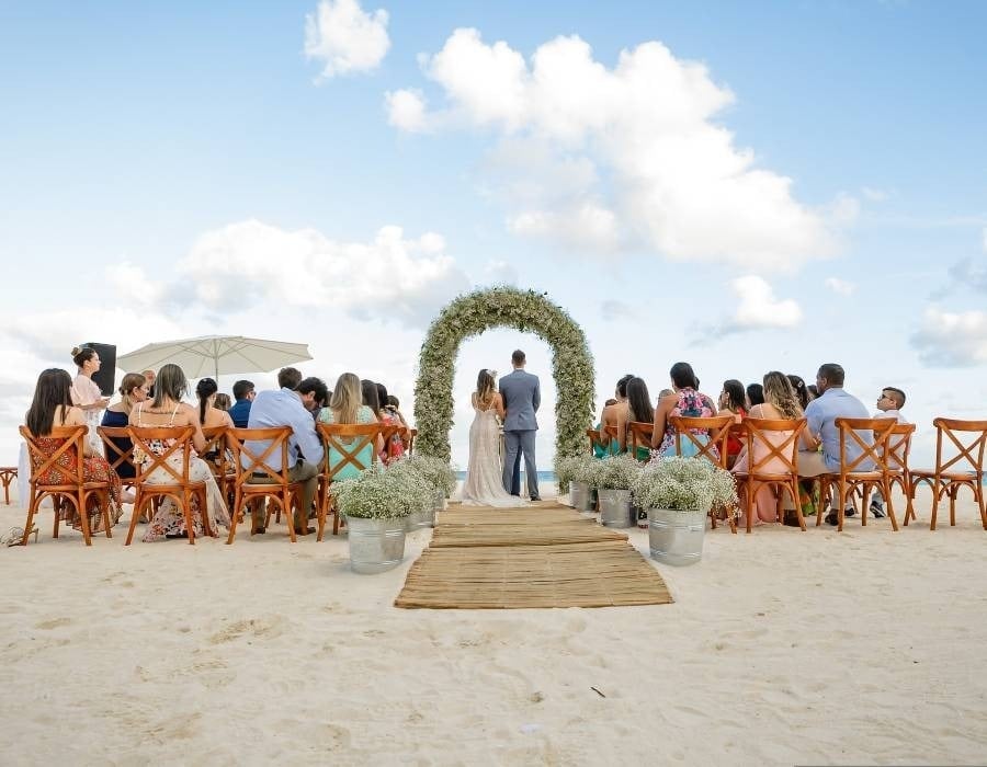 Bride and groom at altar decorated with flowers and seated guests, celebrating the wedding on a Mexican beach in Park Love
