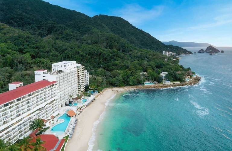 an aerial view of a hotel on a tropical beach with mountains in the background .