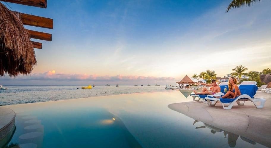 Casal na piscina infinita com vista para o mar, ao pôr do sol no Hotel Grand Park Royal Cozumel