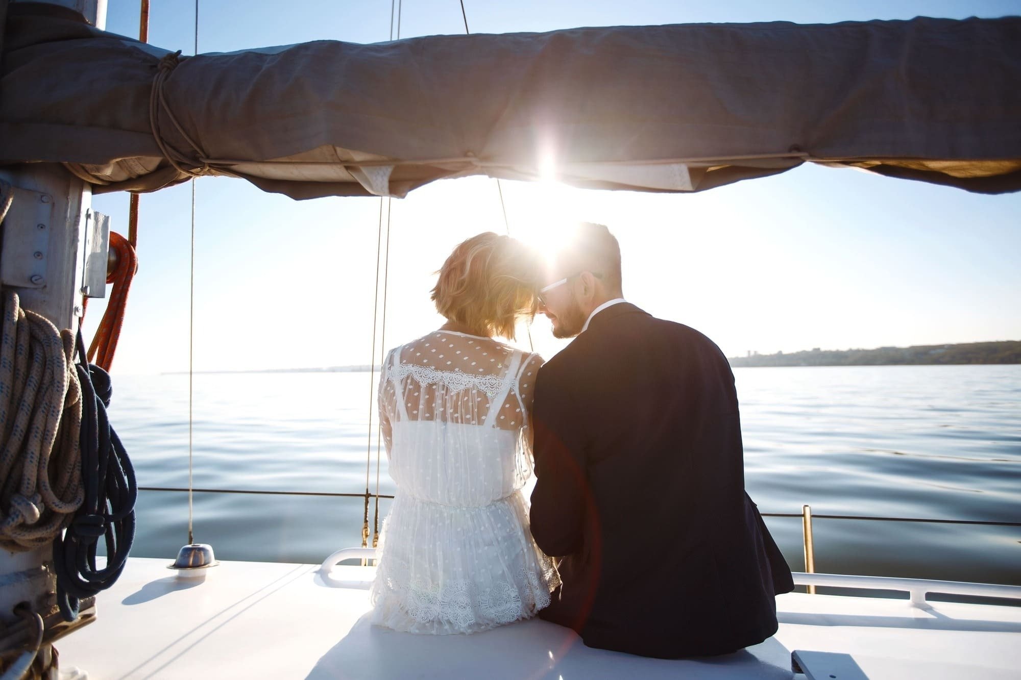 uma noiva e um noivo em um barco olhando para o sol