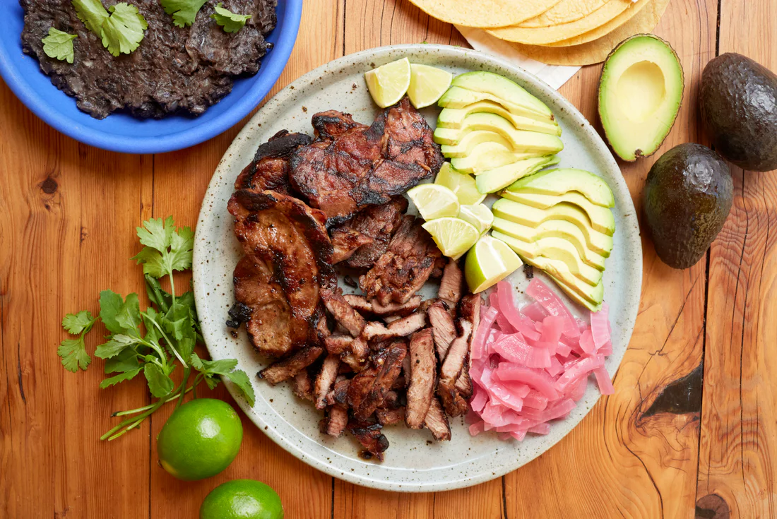 un plato de carne con aguacate y cebollas moradas sobre una mesa de madera