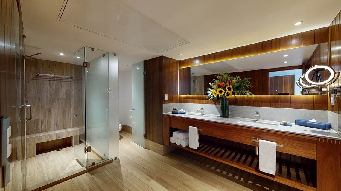 Cuarto de baño con ducha, espejo y jarrón de flores del Hotel Grand Park Royal Puerto Vallarta
