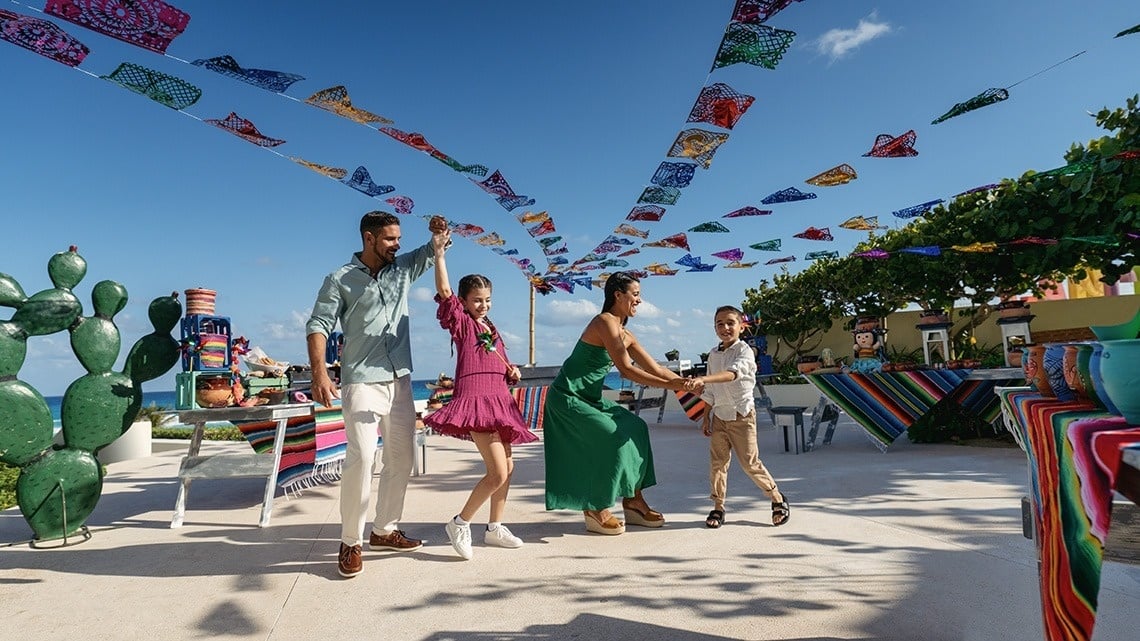 uma família está dançando em um pátio com bandeiras coloridas ao fundo