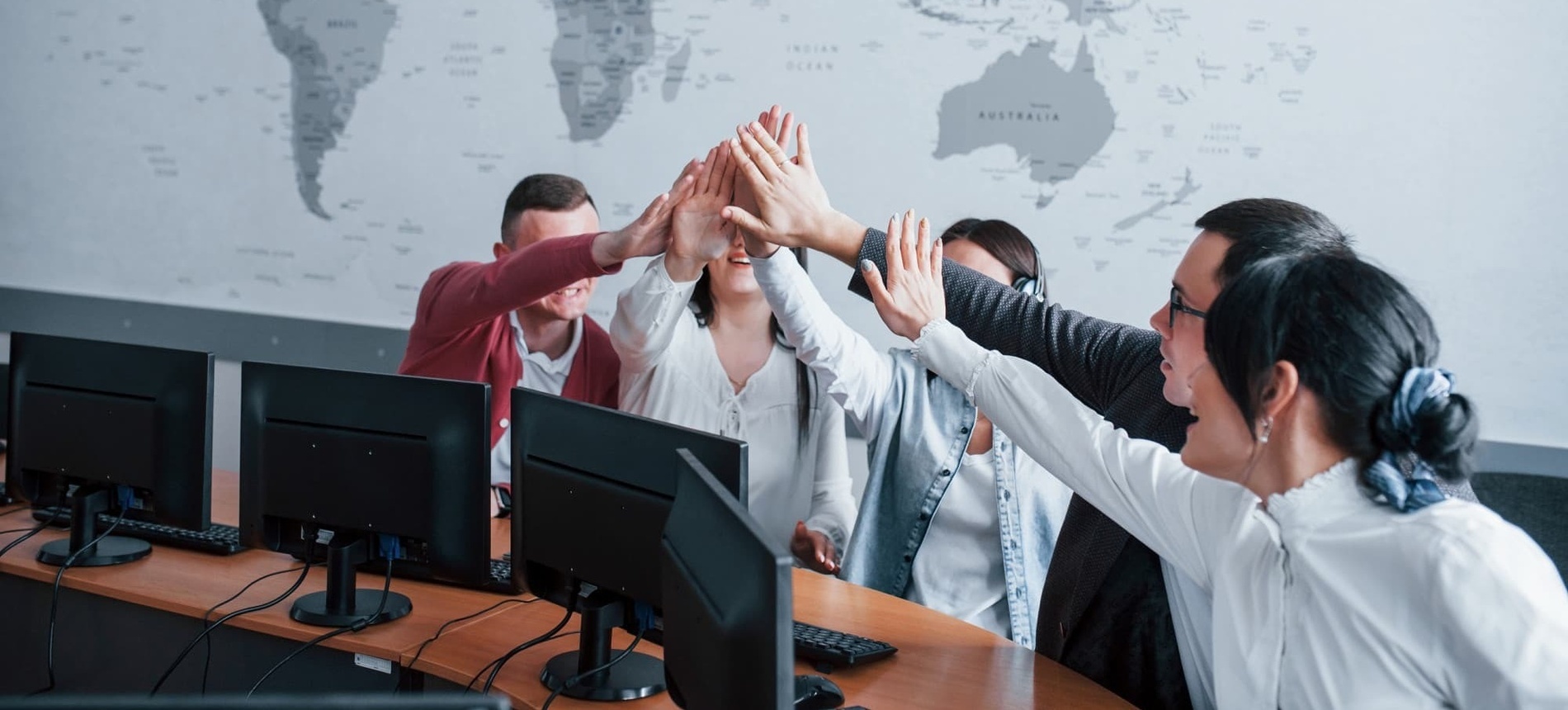 um grupo de pessoas dão um high five em frente a um mapa do mundo