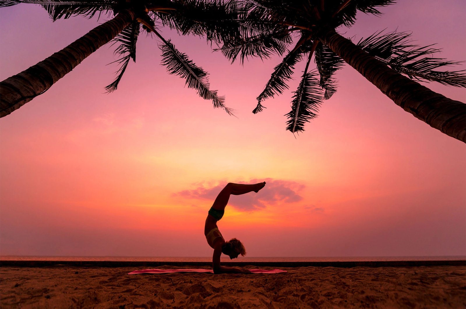 a woman is doing a handstand on the beach at sunset