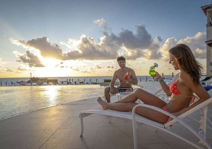 un hombre y una mujer están sentados en sillas junto a una piscina al atardecer .