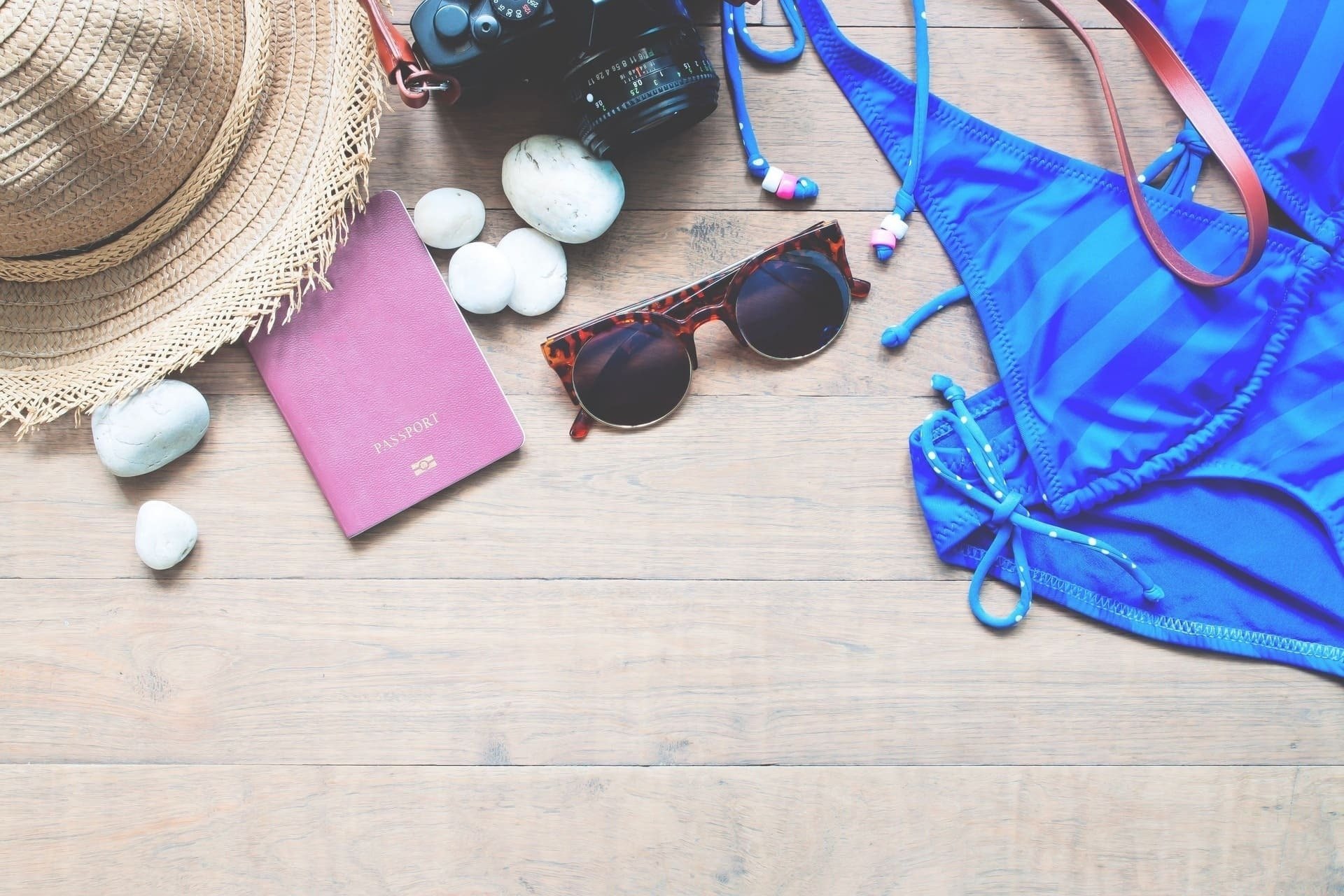 a passport sunglasses a hat and a camera on a wooden table