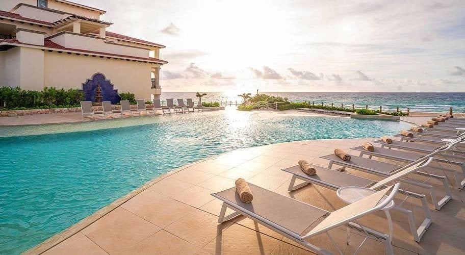 Nascer do sol sobre uma piscina ao ar livre com redes ao lado da praia do Grand Park Royal Cancun Hotel