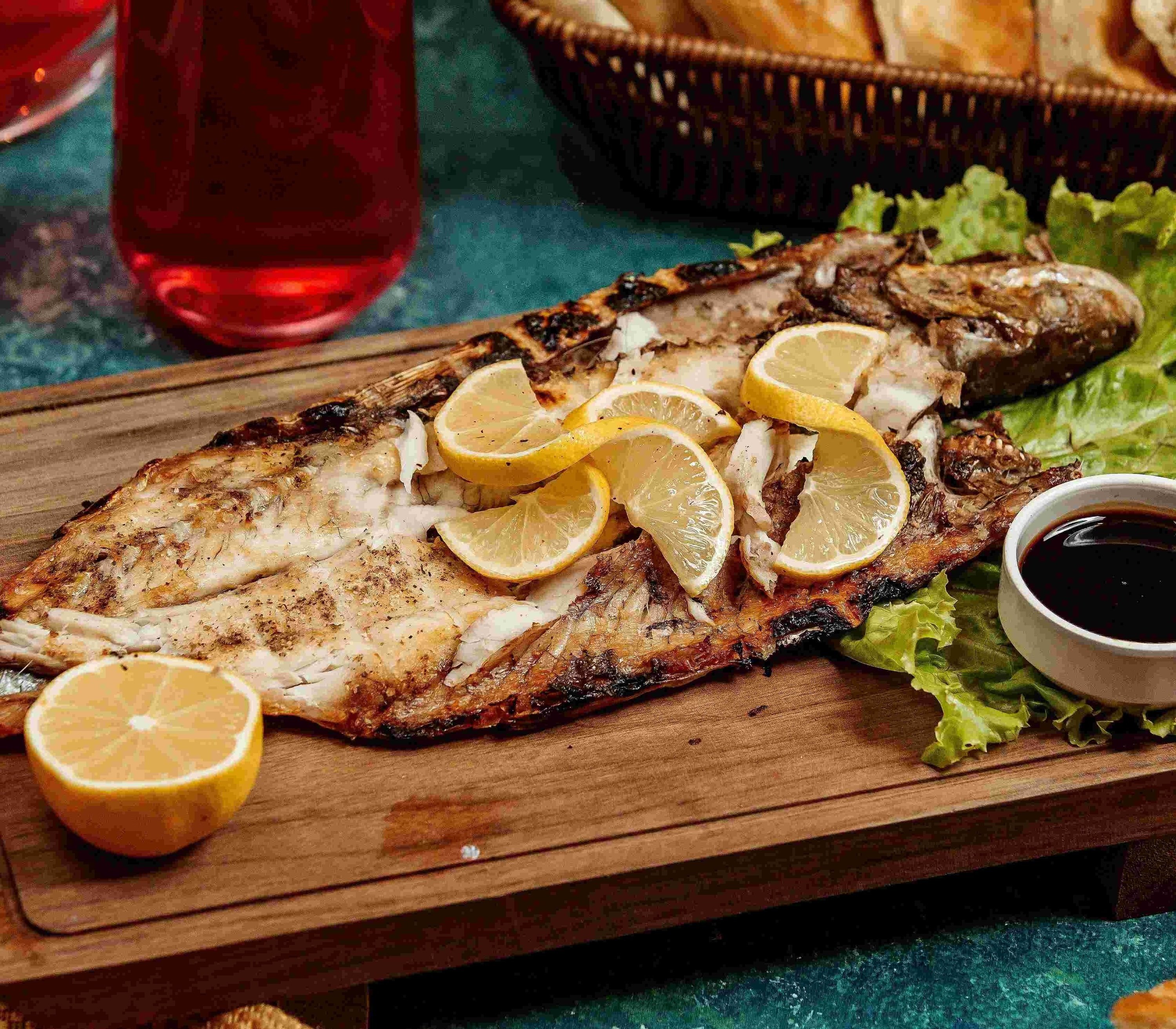 a large piece of grilled fish with lemon slices on a wooden cutting board