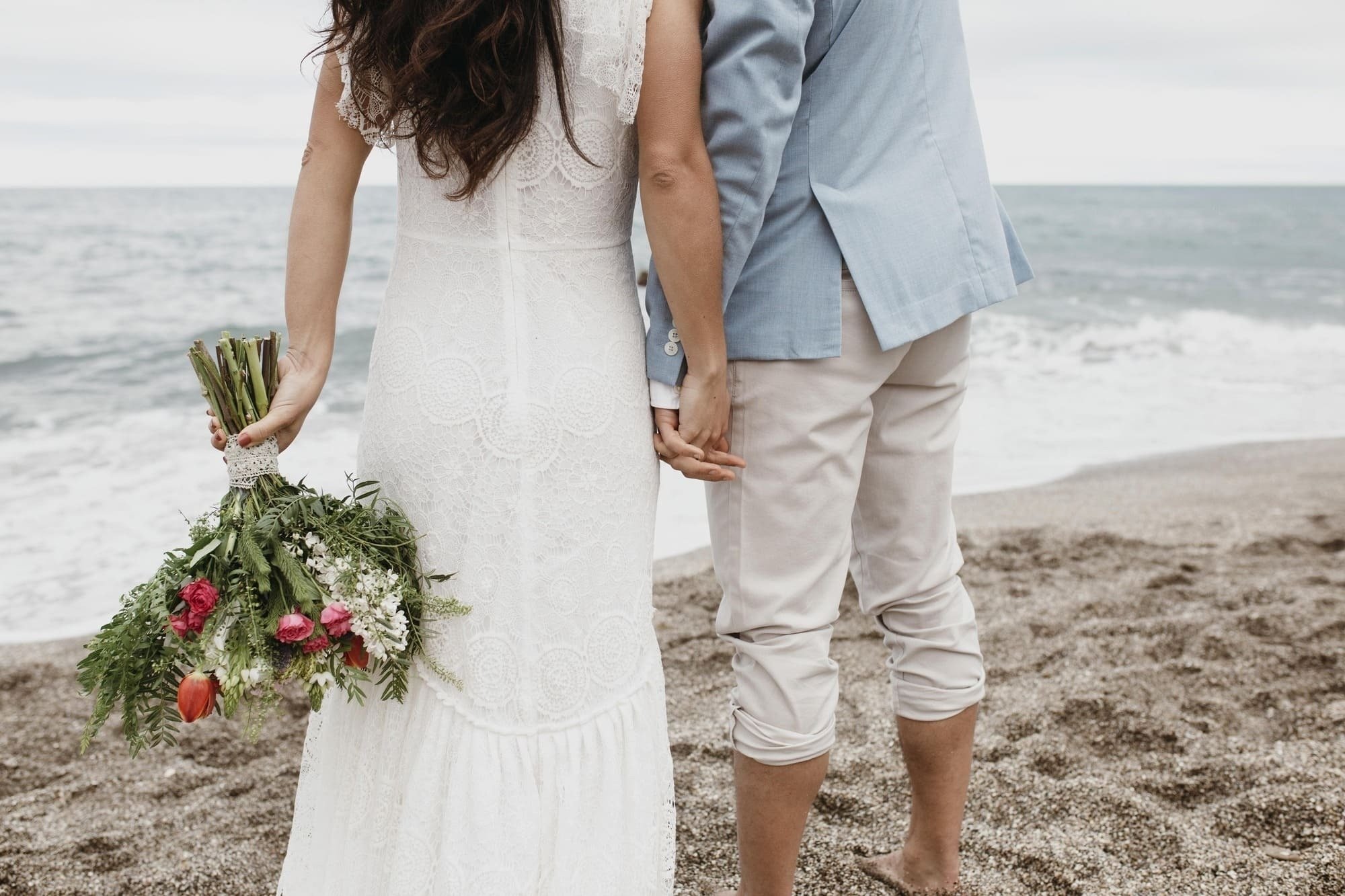 a bride and groom holding hands on the beach