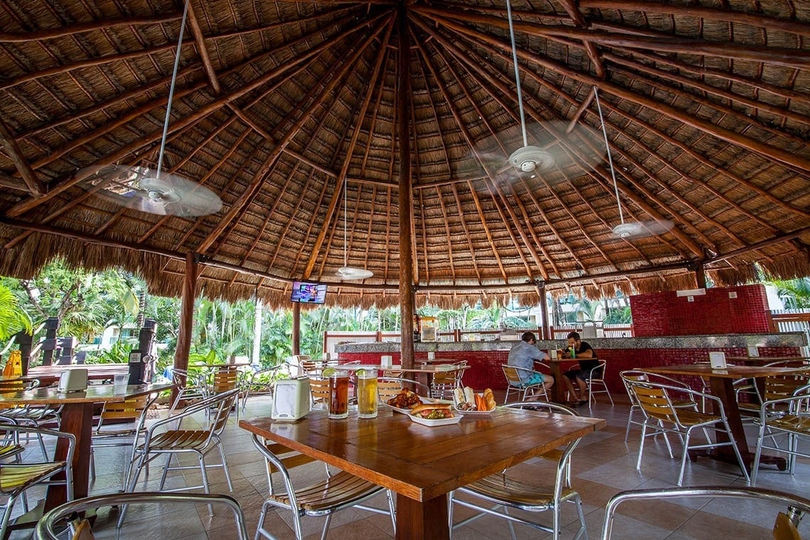 um restaurante com mesas e cadeiras sob um telhado de palha