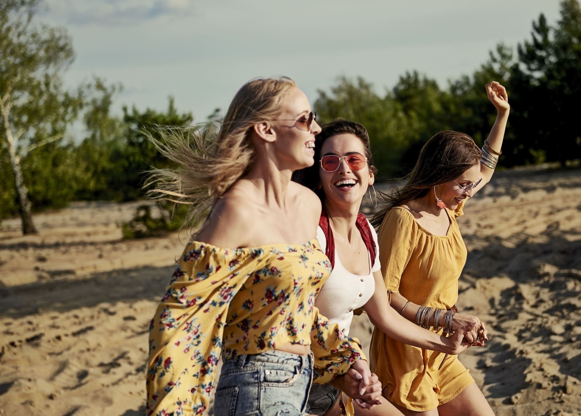 three women are holding hands and laughing while walking on a sandy beach