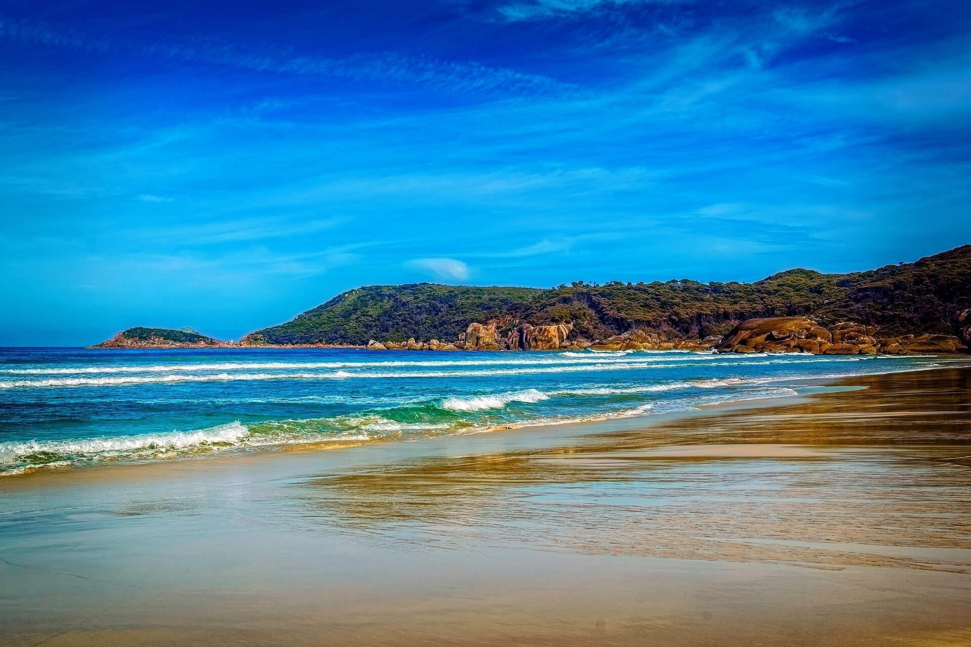 a beach with a mountain in the background and waves crashing on the sand