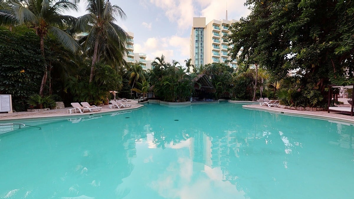 Piscina exterior con isla de plantas tropicales en el centro en Park Royal Grand Cozumel