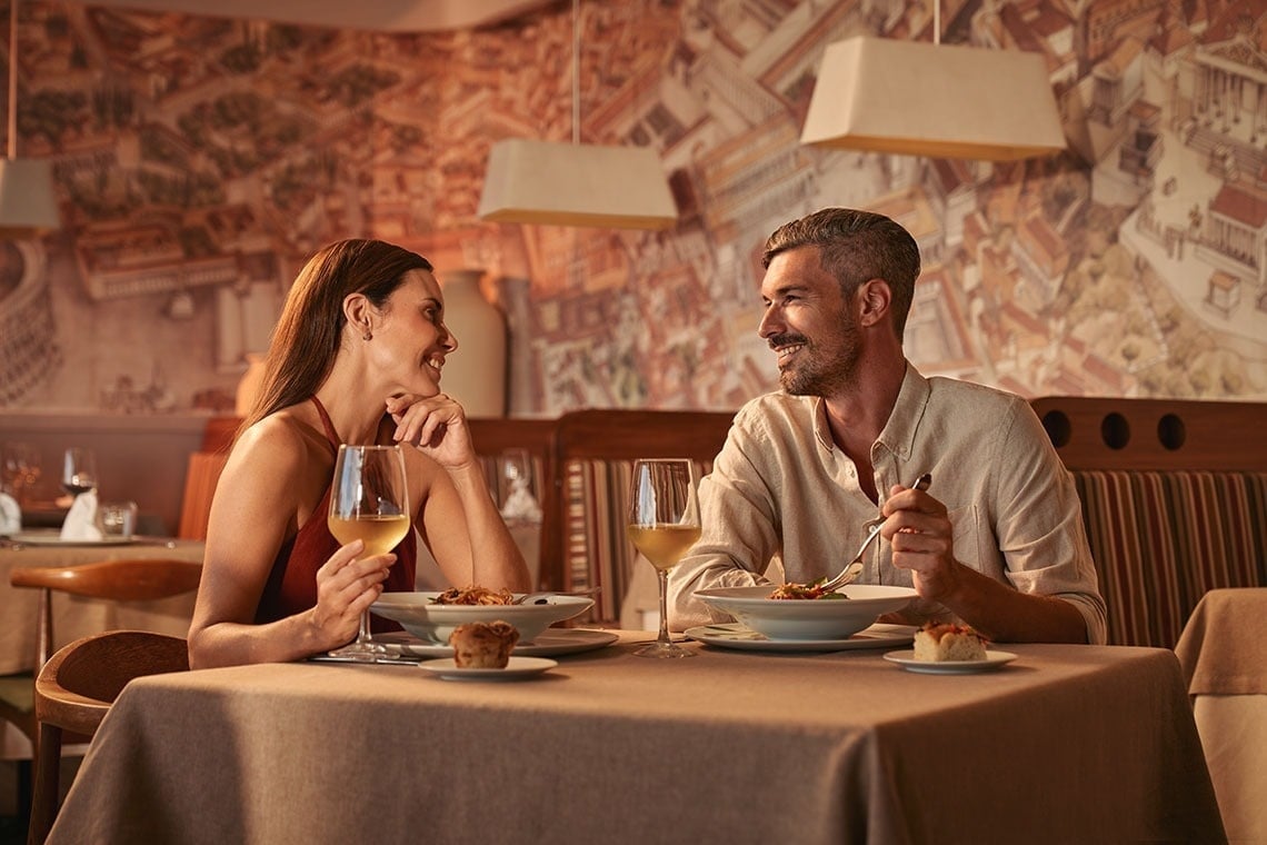 a man and woman are sitting at a table with plates of food and glasses of wine