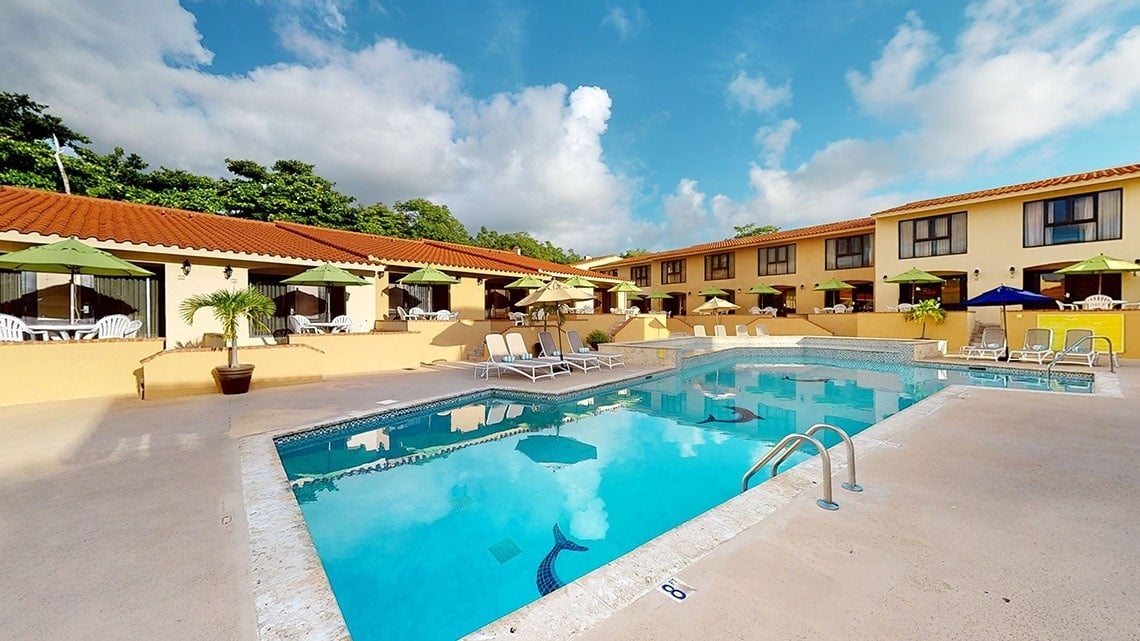 a large swimming pool in front of a hotel with chairs and umbrellas