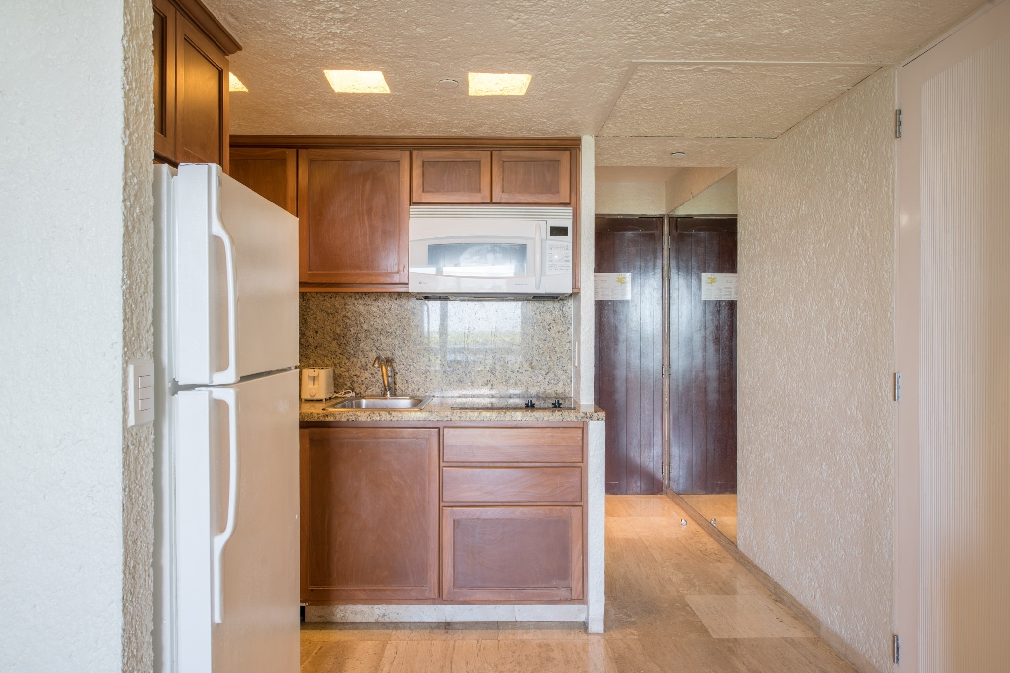 Compact kitchen at Park Royal: Club Regina Cancun, featuring a white refrigerator, microwave, and cabinets.