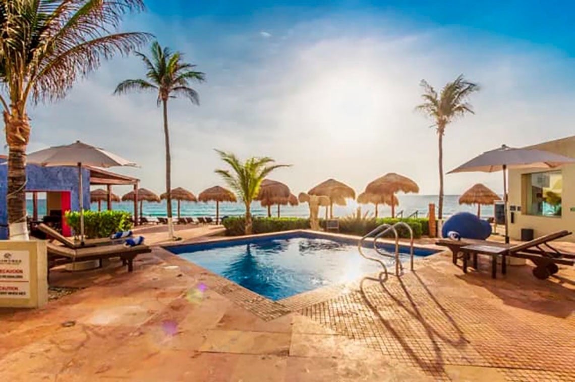 Piscina y playa en Park Royal: Club Regina Cancún con palmeras y sombrillas.