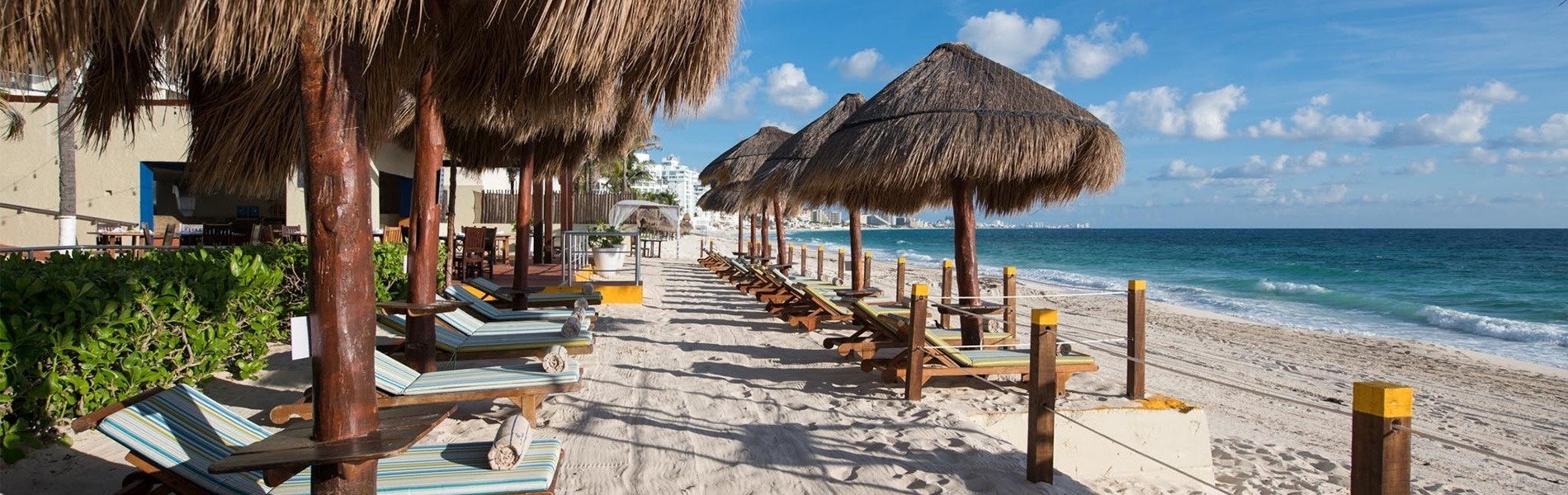 Beach loungers under thatched umbrellas at Park Royal: Club Regina Cancun.