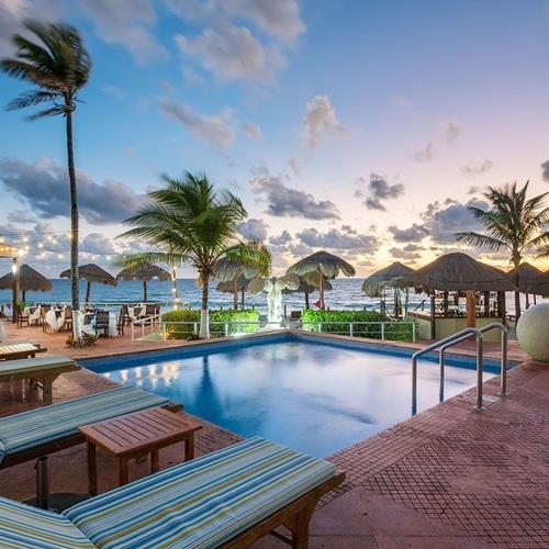 Piscina y comedor exterior en Park Royal: Club Regina Cancún al atardecer.