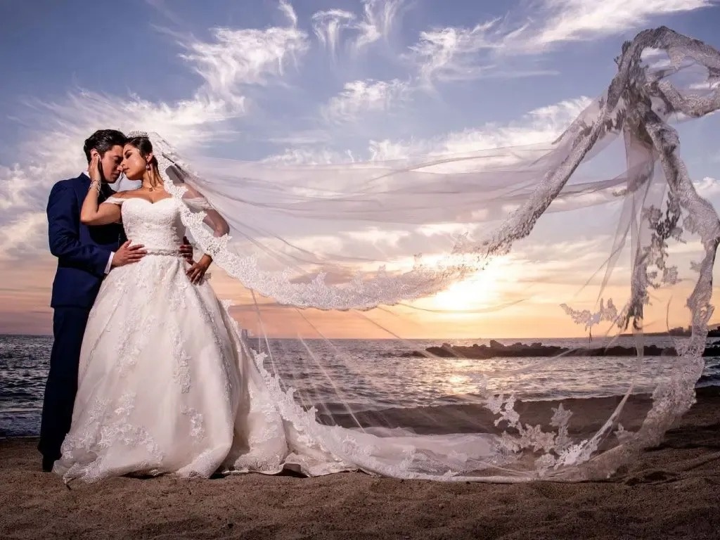 Pareja de novios en boda en la playa, con velo volando, en Park Royal: Club Regina Puerto Vallarta.