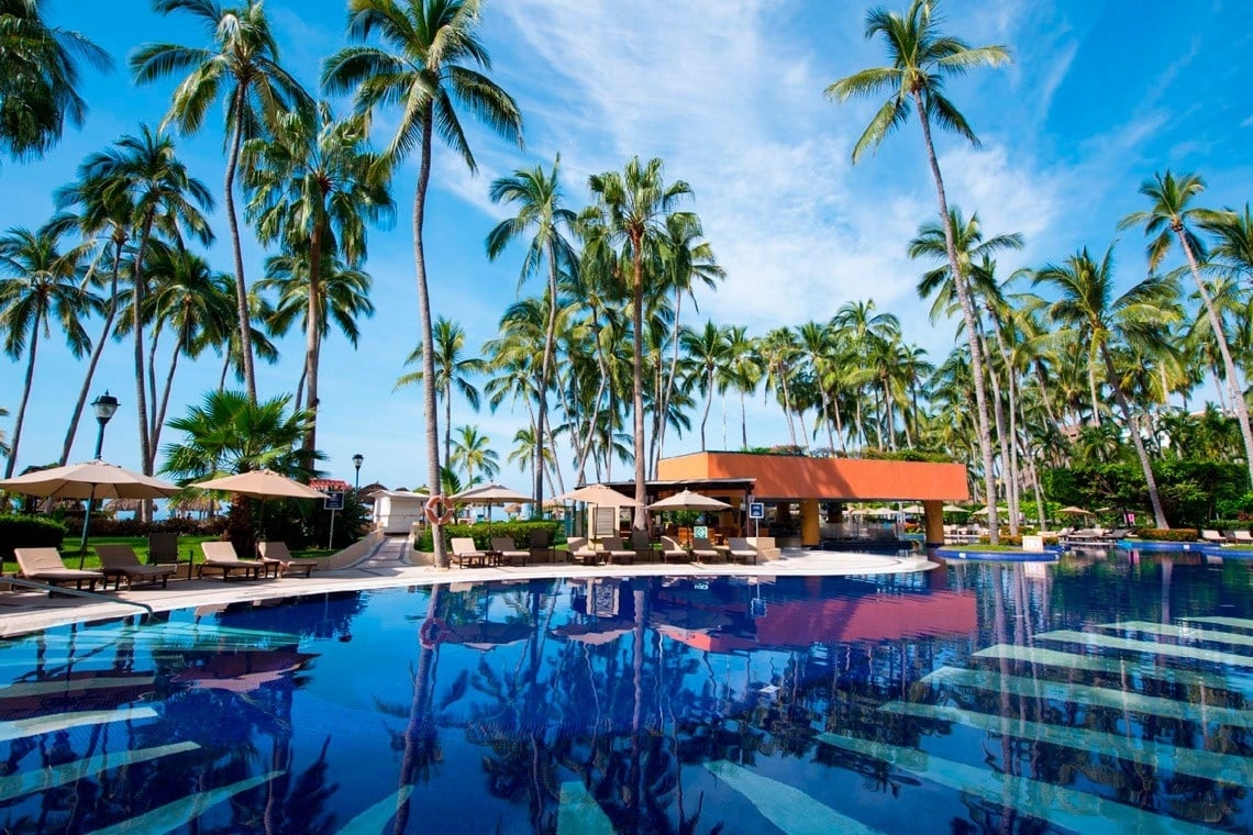 Piscina cristalina en Park Royal: Club Regina Puerto Vallarta, rodeada de palmeras y sol.