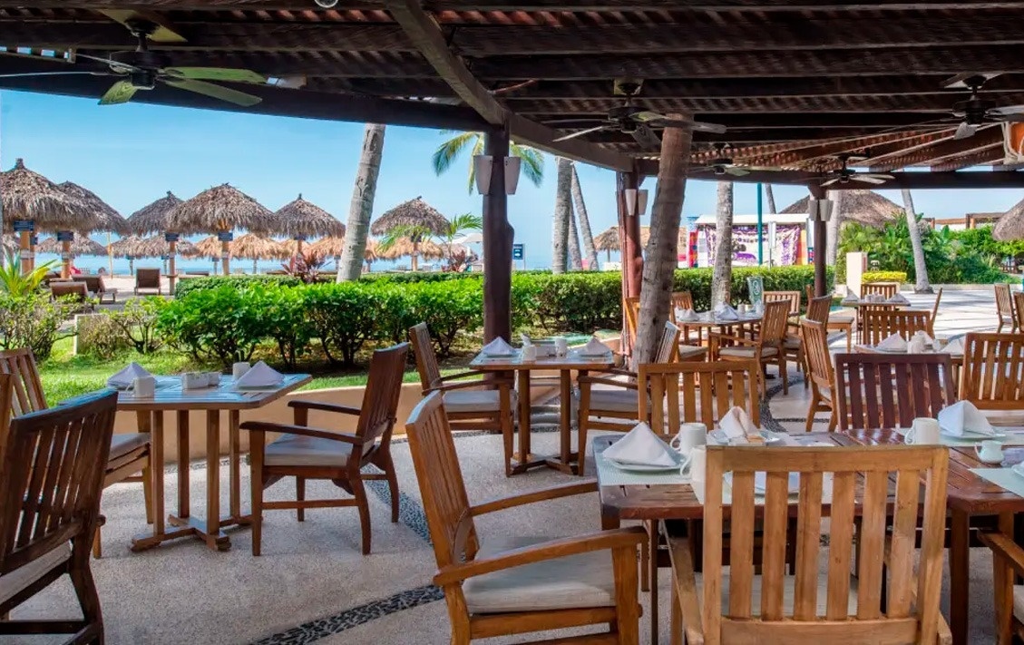 Terraza al aire libre en Park Royal: Club Regina Puerto Vallarta con mesas y sillas de madera frente al mar.