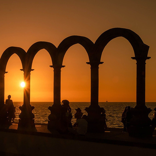 Atardecer en Park Royal: Club Regina Puerto Vallarta, siluetas bajo arcos frente al mar.