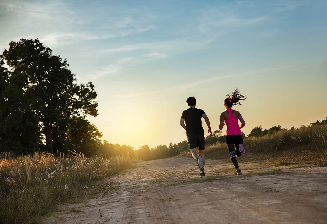 Casal correndo em trilha no pôr do sol. Atividade Pato: Corporativa para bem-estar.