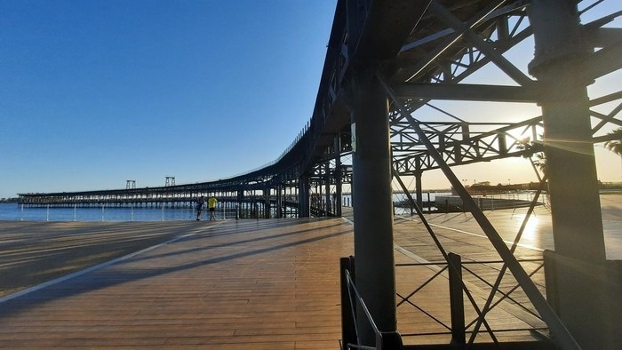 Pôr do sol dourado no cais histórico, com passarela. Perfeito para Pato: Corporativa.