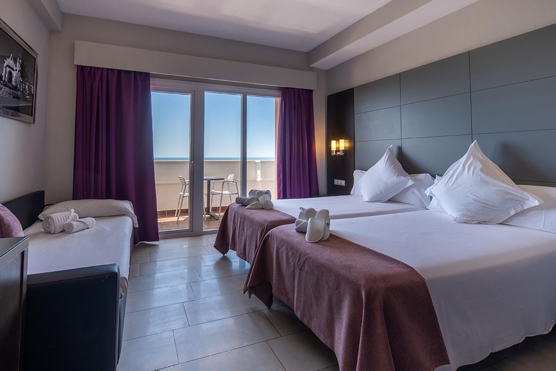 una habitación con dos camas y una ventana con cortinas moradas